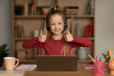 İki eliyle başparmak hareketi yapan liseli kız evdeki masada oturan çevrimiçi sınıfı onaylayan bir dizüstü bilgisayar kullanıyor. E-öğrenmeyi, interneti ve eğitim kavramını seviyorum. Seçici Odaklanma