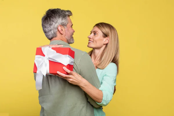 Loving Middle Aged Spouses Hugging Yellow Background Lady Holding Gift — Foto de Stock