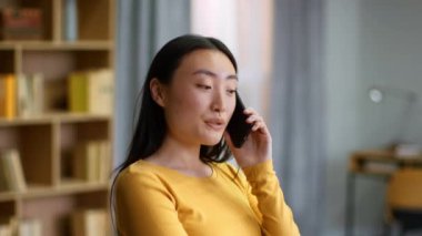 Mobile communication. Close up portrait of young happy carefree asian woman talking on cellphone with friends, enjoying pleasure talk at home, slow motion, free space