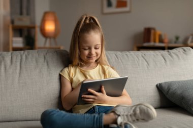 Mutlu Kız Evdeki Koltukta Oturan Dijital Tablet Kullanıyor. Oturma odasındaki bilgisayarda oyun oynayan bir çocuk var. Çocuklar ve Gadget Kavramı. Seçici Odaklanma