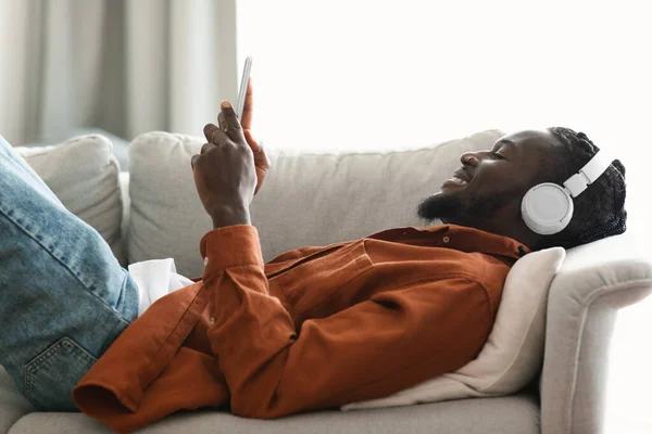 Side View Black Man Listening Music Smartphone Online Resting Couch — ストック写真