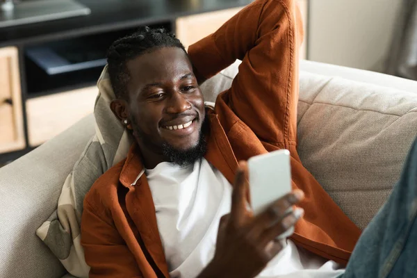 Happy African American Man Using Smartphone Browsing Internet While Lying — Stockfoto
