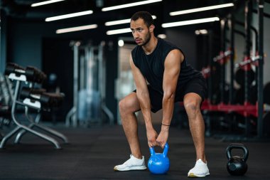 Motivated Young Black Man Training With Kettlebell At Modern Gym Interior, Handsome Muscular African American Bodybuilder Lifting Heavy Dumbbell While Exercising In Sport Club, Copy Space