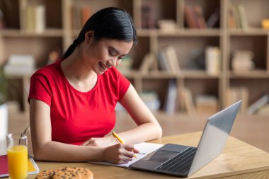 Knowledge and homework. Smiling young asian female student with laptop watching online lesson in room interior. Lecture, education at home, study and social distance, prepare to test due covid-19