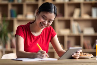 Education at home and new app. Cheerful young asian girl student doing homework with tablet, watch online lesson in room interior. Study, new normal and knowledge, exam preparation and video call