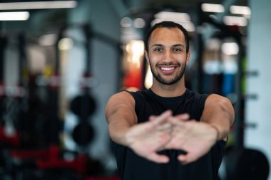 Handsome Smiling Black Man Stretching Arms Before Training In Gym, Closeup Portrait Of Sporty Athletic African American Guy Warming Up His Hands During Workout In Modern Fitness Club, Selective Focus
