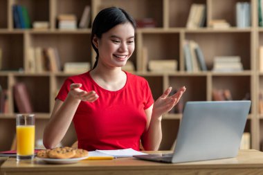 Smiling teen chinese lady female student studying with laptop, watching online lesson in room interior. Education at home, social distancing with modern device, video call during covid-19 quarantine