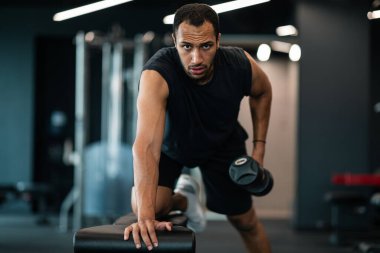 Muscular african american man doing biceps workout with dumbbell in gym, motivated sporty black guy training with light weights at modern sport club, enjoying bodybuilding and healthy lifestyle