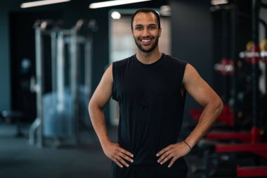 Portrait Of Handsome African American Male Athele Posing In Gym Interior, Happy Muscular Black Man Standing In Modern Fitness Club And Smiling At Camera, Enjoying Bodybuilding And Healthy Lifestyle