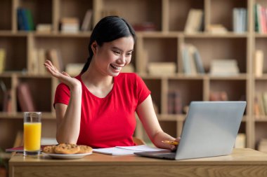 Glad teenager japanese lady student say hello, waving hand, watching online lesson in room interior. Hi and greeting, education at home, video call, meeting and new normal during covid-19 outbreak
