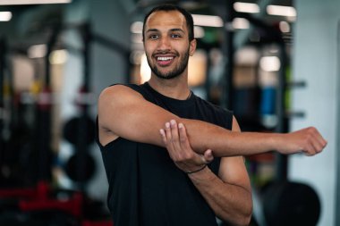 Handsome Young African American Man Warming Up Before Workout In Gym, Muscular Black Male Athlete Stretching Arms While Training In Modern Sport Club, Closeup Portrait, Selective Focus