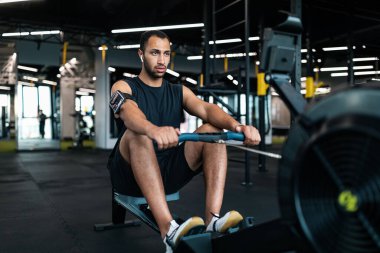 Sporty Young Black Man Exercising With Rowing Machine At Modern Gym, Motivated African American Male Athlete Training In Fitness Club Interior, Enjoying Healthy Lifestyle, Closeup Shot, Copy Space