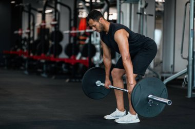 Sporty Black Man Lifting Heavy Barbell While Training At Gym, Muscular African American Bodybuilder Making Deadlift Weight Exercise While Working Out At Modern Sport Club Interior, Copy Space