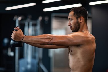 Side View Of Muscular Shirtless Black Man Training With Kettlebell At Gym, Young African American Male Athlete Lifting Heavy Dumbbell While Exercising In Modern Sport Club, Copy Space