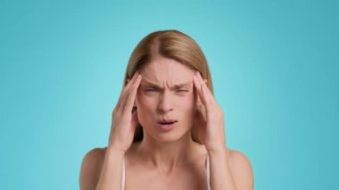 Migraine concept. Close up portrait of middle aged woman suffering from acute headache, massaging her painful temples, blue studio background, slow motion
