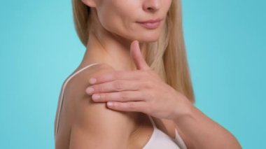 Body pampering concept. Close up shot of unrecognizable caucasian woman rubbing healing gel to her shoulder, blue studio background, slow motion