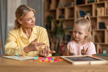 Smart girl counting on fingers, studying with private teacher in office, kid learning the numbers and how to count, sitting at desk with female tutor