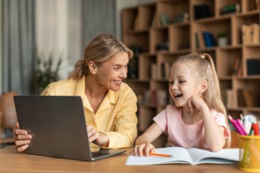 Online education. Happy mom and her little daughter using laptop, mother helping female child with homework and remote study, enjoying distance learning