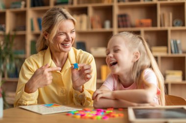 Speaking classes for kids. Happy teacher showing letter R to laughing girl, exercising together at classroom and smiling, enjoying lessons