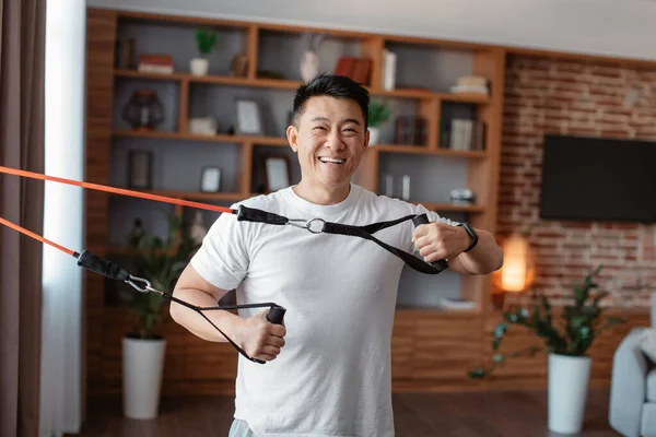 Home fitness. Happy asian man exercising using resistance rubber band, training in living room at home. Workout equipment and sporty lifestyle concept