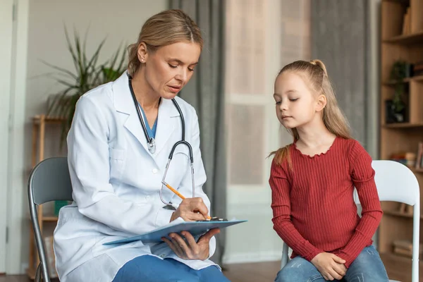 Focused Female Doctor Writing Girls Symptoms Clipboard While Child Looking — Photo