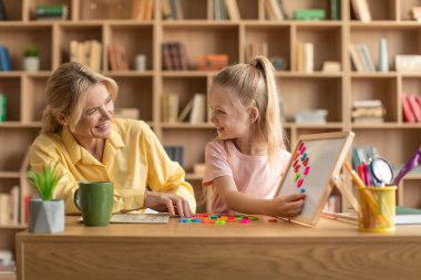 Preschool education. Happy professional female teacher exercising with pretty girl, cute child reading English letters and making words on whiteboard