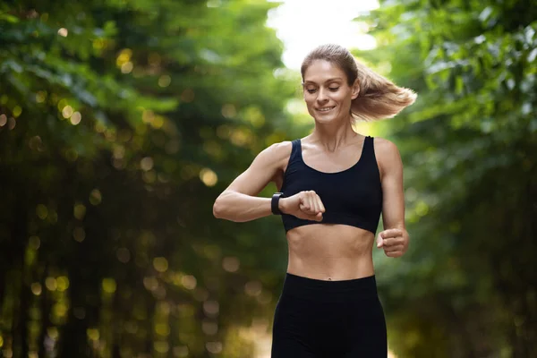 Sporty Blonde Lady Looking Fitness Bracelet While Running Alone Outdoors — ストック写真