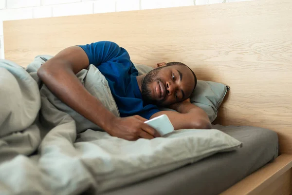 African American Guy Using Phone Texting Lying Modern Bedroom Indoor — 图库照片