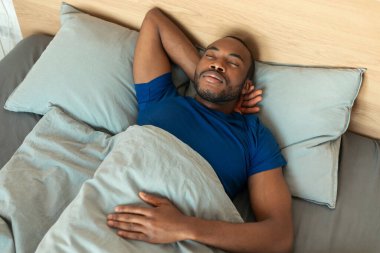 High Angle Shot Of Sleeping Black Man Napping Peacefully Resting In Modern Bedroom At Home. Asleep Guy Lying In Bed. Healthy Sleeping Routine Concept. Above View