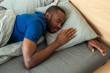 Above View Of Sleeping African American Man Lying Resting Head On Pillow In Modern Bedroom At Home. Black Guy Napping In Bed Indoor. Rest And Recreation. Selective Focus