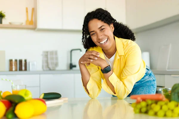Portrait of excited african american lady posing at kitchen interior, looking at camera and smiling, young black woman having breakfast at home