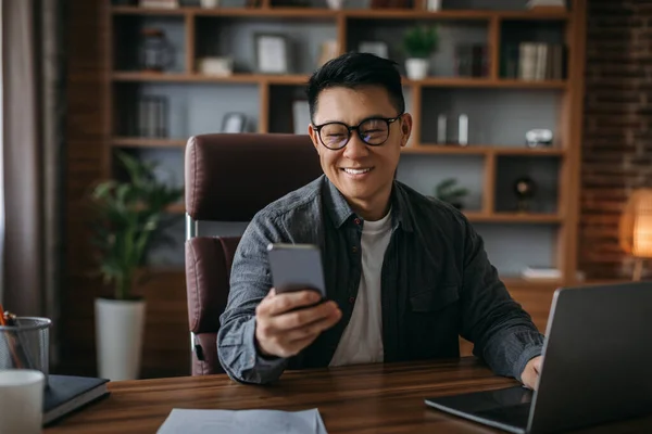 Glad Mature Korean Male Glasses Reads Message Smartphone Work Laptop — Stock Photo, Image