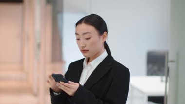 Life online. Young asian woman manager web surfing on smartphone, reading social media news on cellphone, standing at office corridor, slow motion, free space