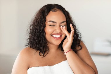 Natural essential beauty. Joyful black plus size lady with closed eyes touching her soft flawless skin, laughing and enjoying result of costmetology treatment,