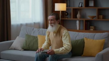 Football streaming. Happy emotional senior bearded man supporting sport team, watching game on tv at home, laughing and jumping on sofa, slow motion, empty space