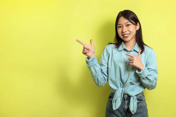 Happy Chinese Woman Pointing Fingers Aside At Yellow Background Standing In Studio. Lady Smiling To Camera Advertising Great Offer Showing Copy Space. Advertisement Banner