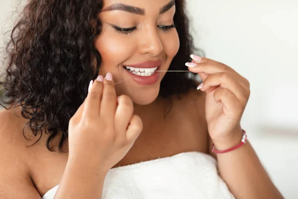 Oral care concept. Young black plus size lady using dental floss, cleansing perfect white teeth, closeup. Happy african american woman making daily hygiene routine at home