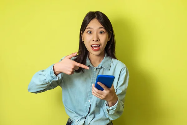 Excited Japanese Lady Pointing Finger Cellphone Looking Camera Standing Yellow — Stok fotoğraf