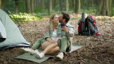 Camping weekend. Happy middle aged loving spouses resting in woodland together, embracing and making selfie on smartphone, slow motion