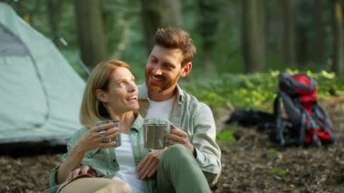 Happy rest. Close up portrait of positive middle aged couple in love drinking tea from metal cups, enjoying camping activity, laughing together, slow motion, free space