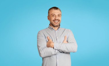 Happy Mature Male Posing Smiling To Camera Standing Crossing Hands On Blue Studio Background. Shot Of Cheerful Middle Aged Man Wearing Casual Clothes. Successful Businessman Concept
