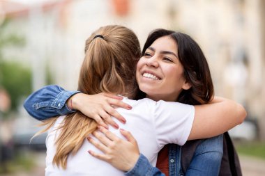 Friendship Concept. Two Joyful Young Female Friends Embracing Outdoors During Meeting On City Street, Cheerful Millennial Ladies Hugging And Laughing, Happy To See Each Other, Closeup Portrait