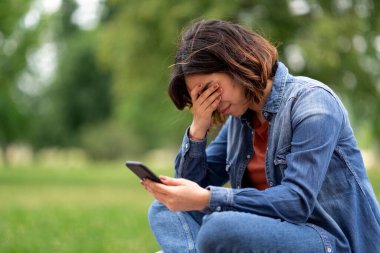 Depressed Young Arab Woman Sitting Outdoors In Park With Smartphone In Hands And Crying, Upset Middle Eastern Female Reading Bad Message, Emotionally Reacting To Brokeup With Boyfriend, Closeup