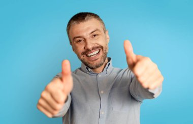 Joyful Middle Aged Male Gesturing Thumbs Up With Both Hands Smiling To Camera Standing Posing Over Blue Background In Studio. I Like And Approve This Offer Concept