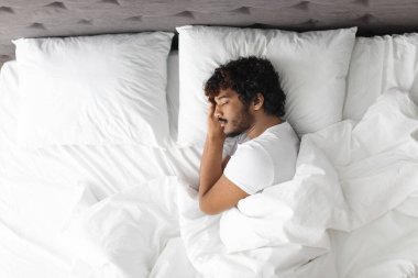 View above of handsome bearded young eastern guy in pajamas resting at home, sleeping on his side with hands under head in comfortable bed., copy space Healthy sleeping concept