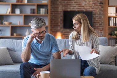 Upset confused adult european husband and wife pay taxes with laptop, suffer from stress and pressure in living room interior. Problems with bills, money, loan and mortgage debts, bankruptcy at home