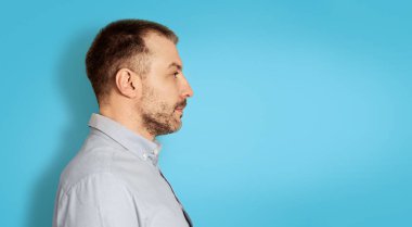Side View Of Serious Middle Aged Man Looking Aside At Empty Space Standing Over Blue Studio Background. Profile Portrait Of Confident Mature Male. Panorama