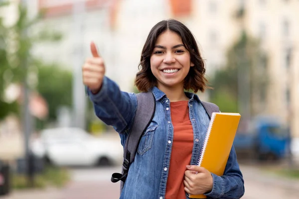 Smiling Arab Female Student Showing Thumb Up Gesture At Camera While Posing Outdoors, Happy Young Middle Eastern Woman Carrying Backpack And Holding Workbooks, Recommending Educational Programs
