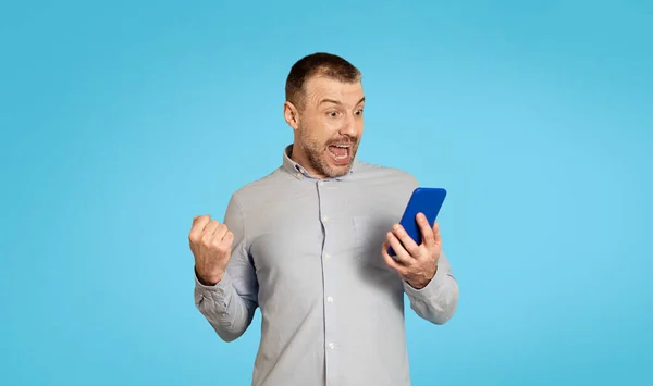 Emotional Middle Aged Man Holding Phone Shaking Fists Standing Blue — Stockfoto