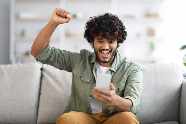 Emotional Curly Millennial Indian Guy Sitting Couch Home Holding Brand — Stockfoto